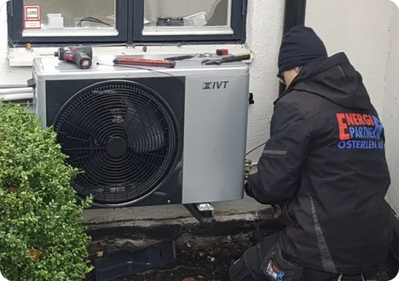 En tekniker i arbete med att serva värmepump eller utföra en nyinstallation utomhus.