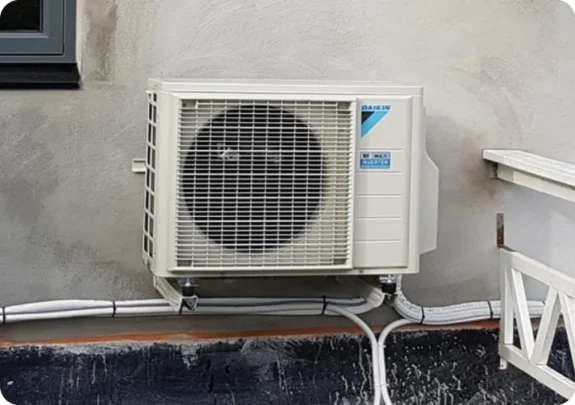 En kompakt luftvärmepump från Daikin monterad med stabila väggfästen på en fasad.